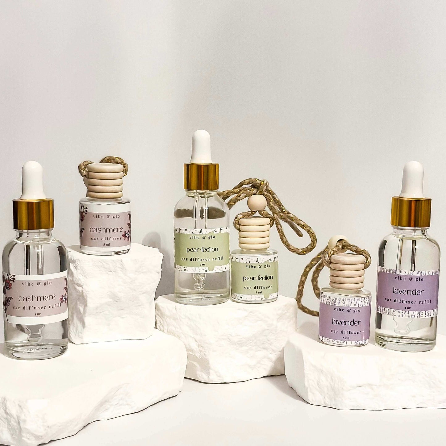 Collection of hanging car diffusers with stylish labels and essential oil scents on white display rocks.