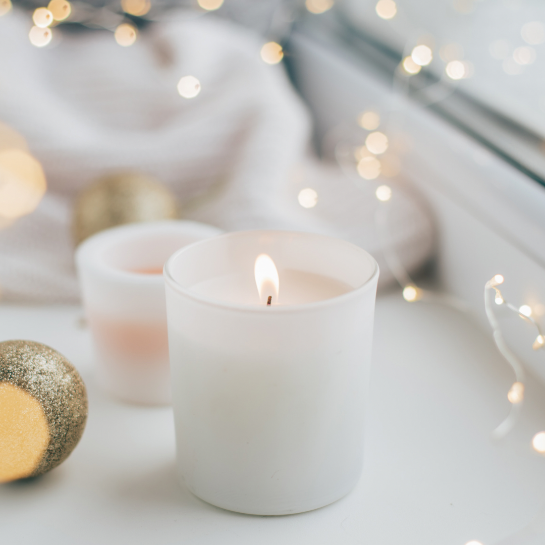 “Cozy white candle surrounded by soft, golden holiday lights and festive ornaments, creating a warm and serene atmosphere for seasonal home decor.