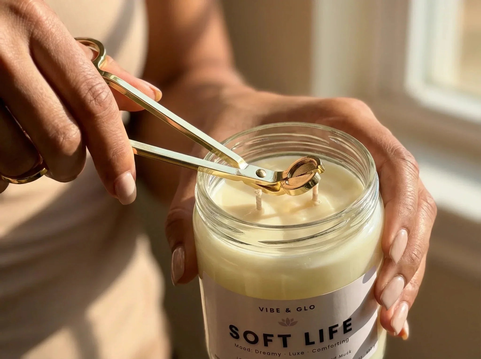 close-up of trimming candle wick with gold wick trimmer on a soy wax glass jar candle for proper candle care and clean burn