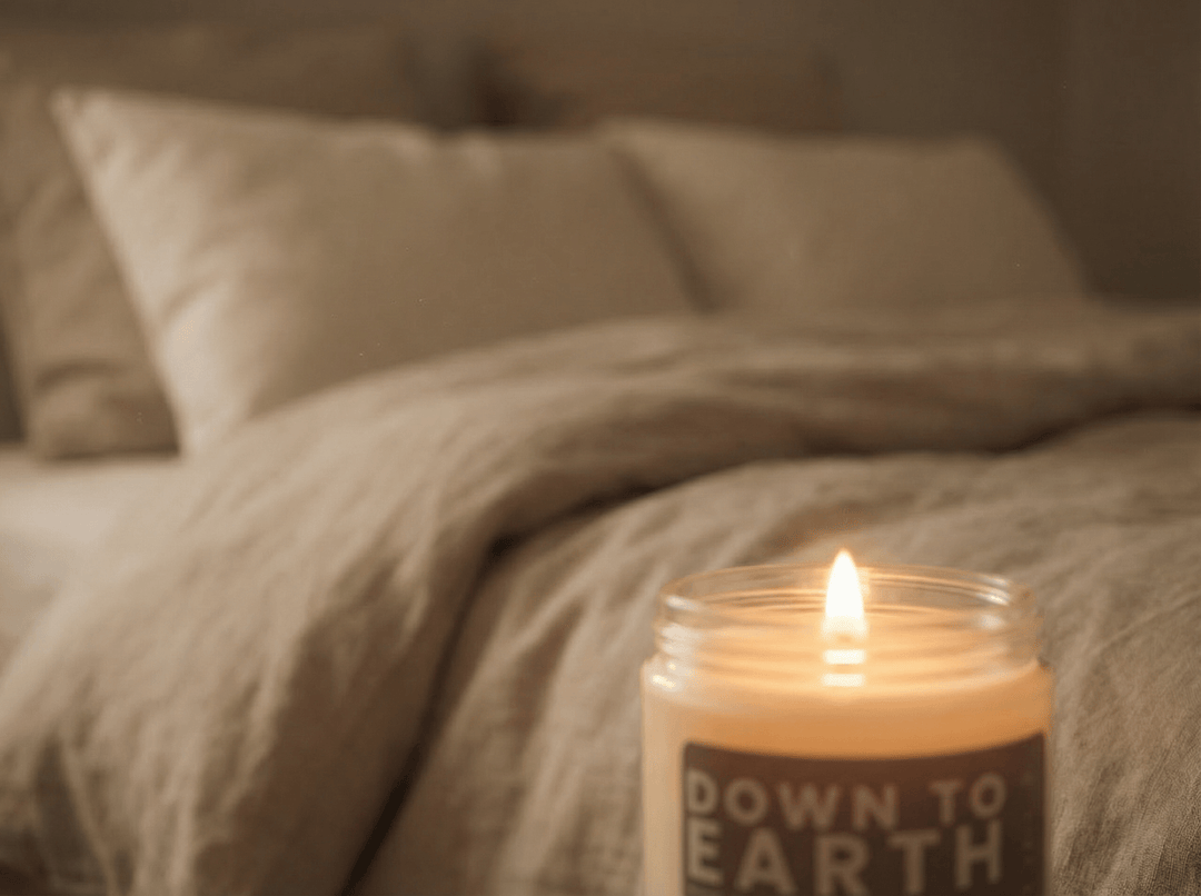 Down to Earth candle glowing beside a bed in a softly lit bedroom, creating a cozy and calming nighttime atmosphere