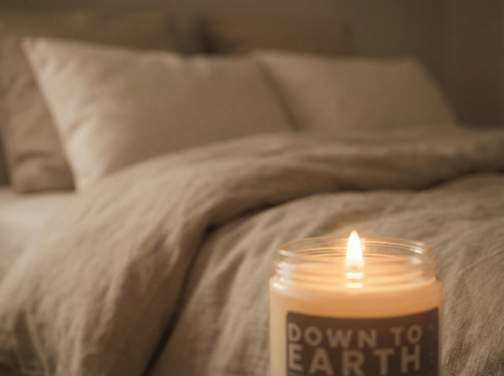 Down to Earth candle glowing beside a bed in a softly lit bedroom, creating a cozy and calming nighttime atmosphere