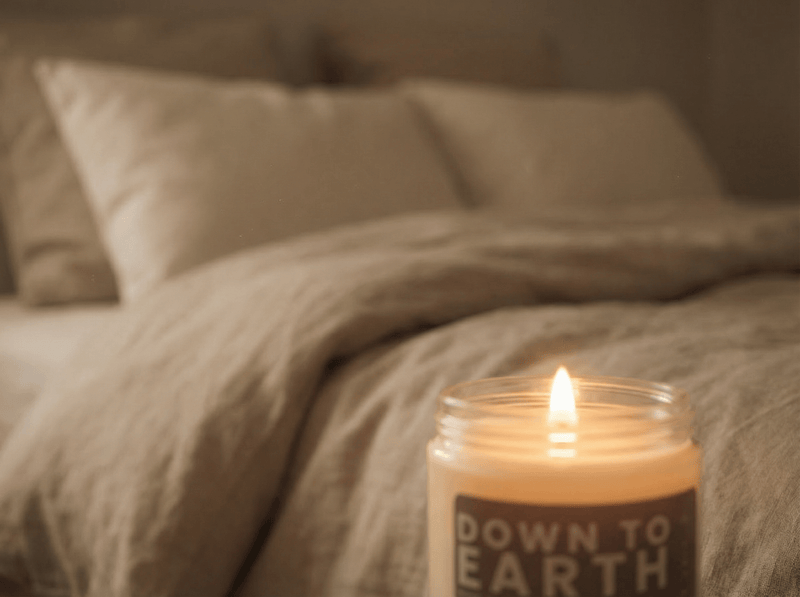 Down to Earth candle glowing beside a bed in a softly lit bedroom, creating a cozy and calming nighttime atmosphere