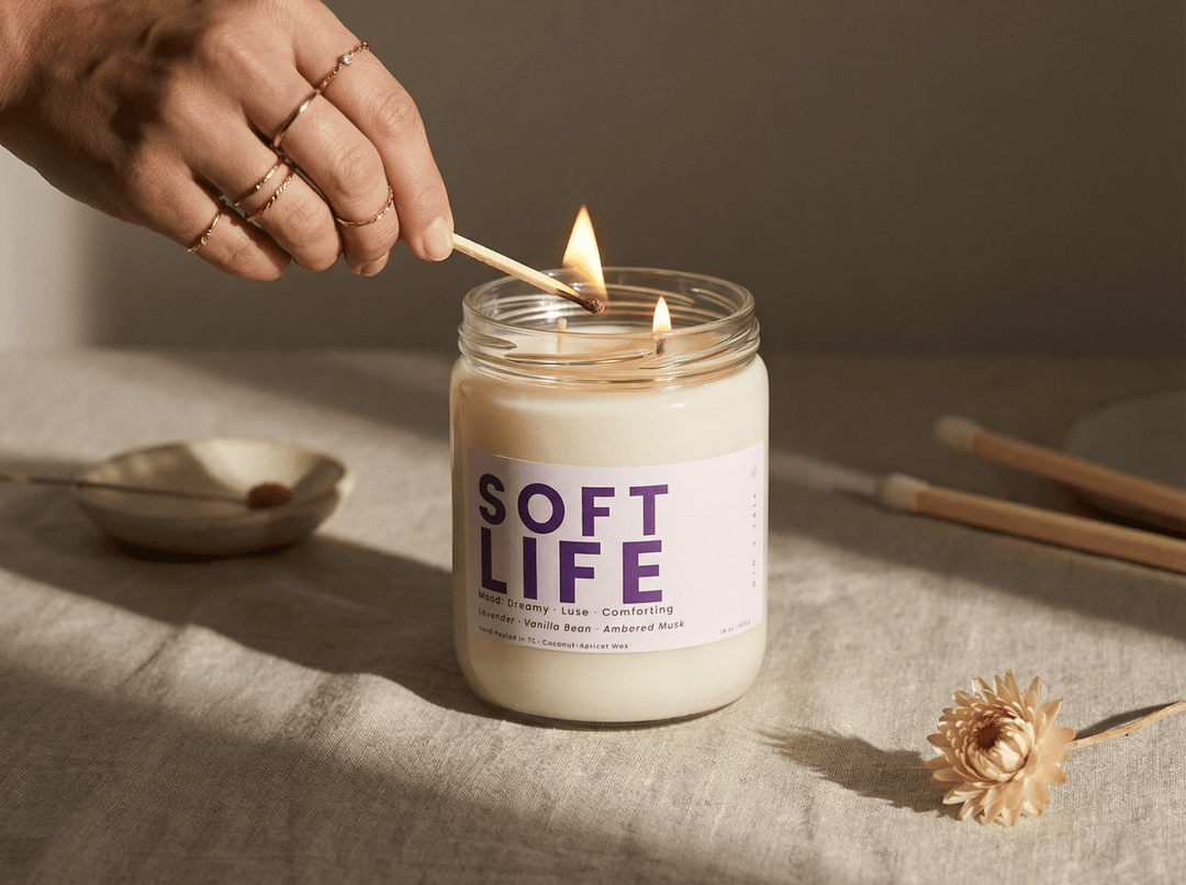 Hand lighting Soft Life candle by Vibe & Glo, representing a calming at-home self-care ritual with soft, warm ambiance