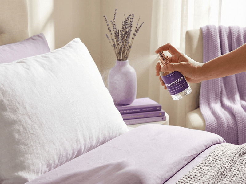 Hand spraying Vibe & Glo Transcend room and linen spray over cozy pillows and lavender decor to make your home smell amazing with clean home fragrance.