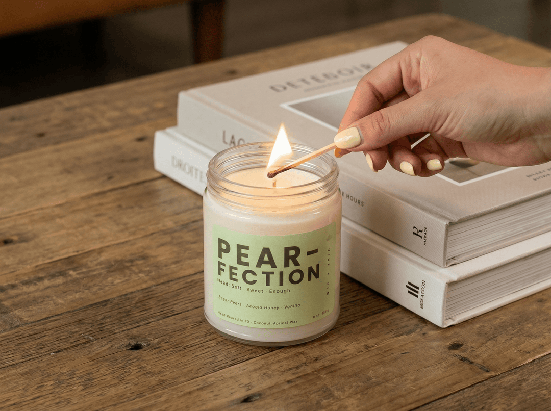 Hand lighting Vibe & Glo Pear-fection scented candle in clear glass jar with coconut apricot wax for a clean burning home fragrance experience