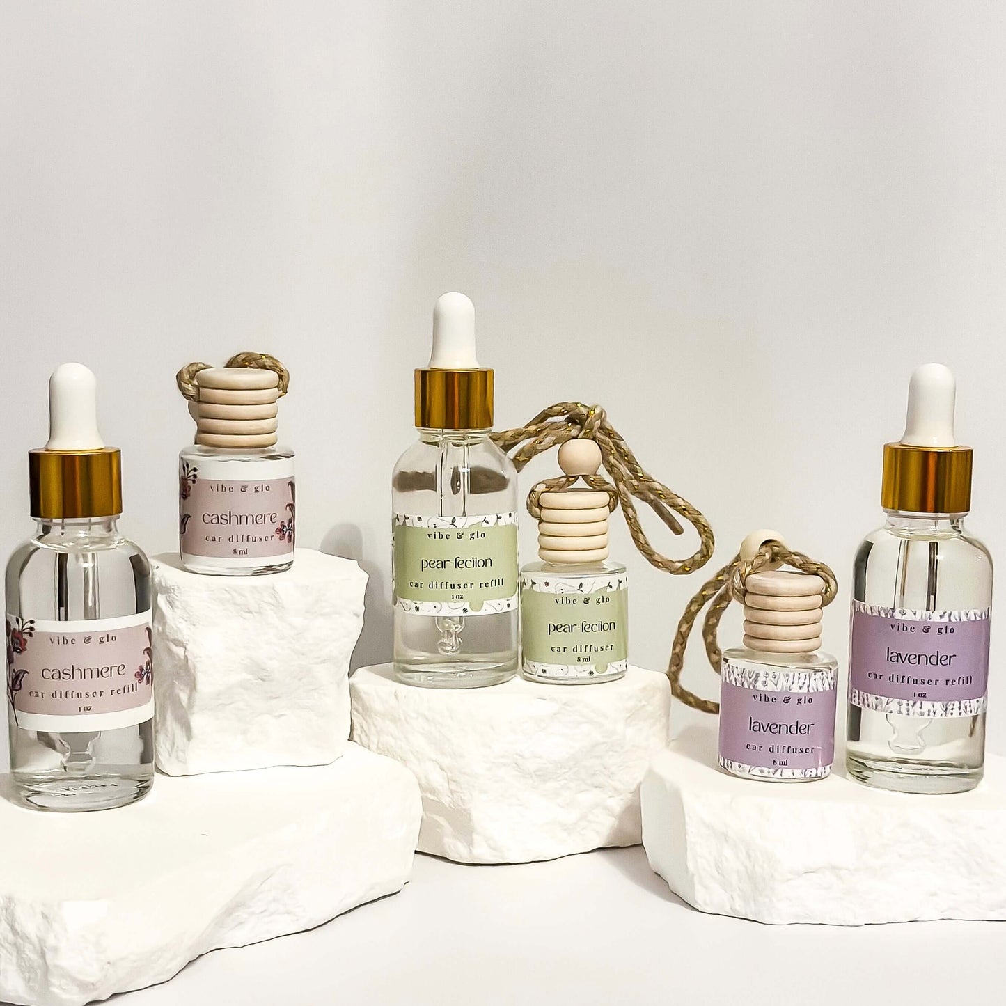 Collection of hanging car diffusers with stylish labels and essential oil scents on white display rocks.