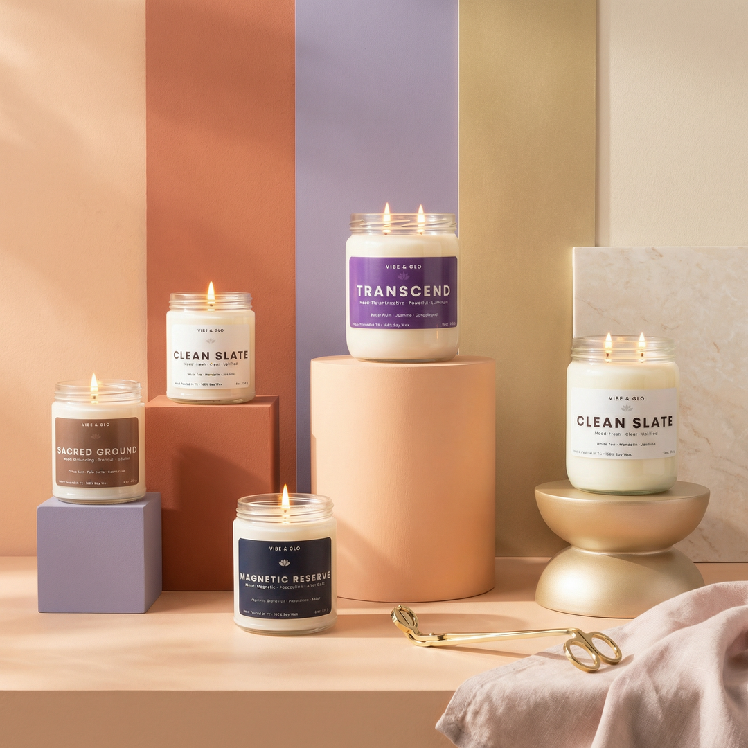 Vibe & Glo candle collection featuring multiple clean-burning soy candles in glass jars displayed on modern pedestals with warm neutral tones, highlighting a range of signature scents for an elevated home fragrance experience.