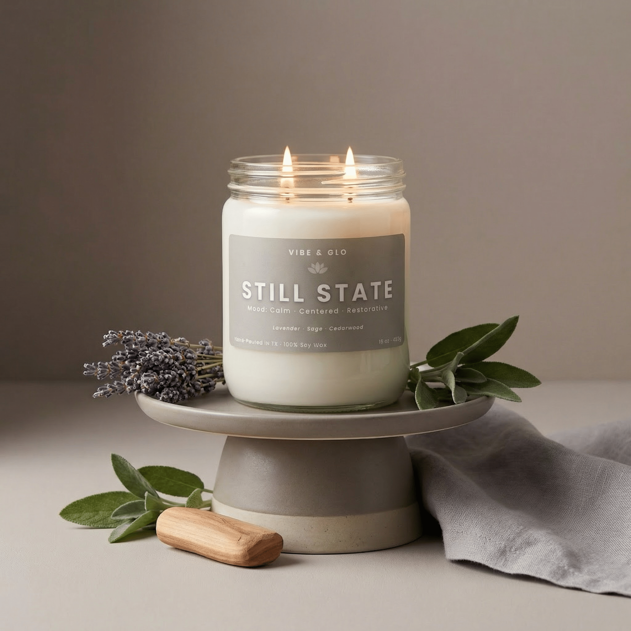 Still State 16 oz double wick soy candle with lavender, sage, and cedarwood notes, lit in a clear glass jar styled with fresh lavender and sage leaves for a calming, large room candle display.