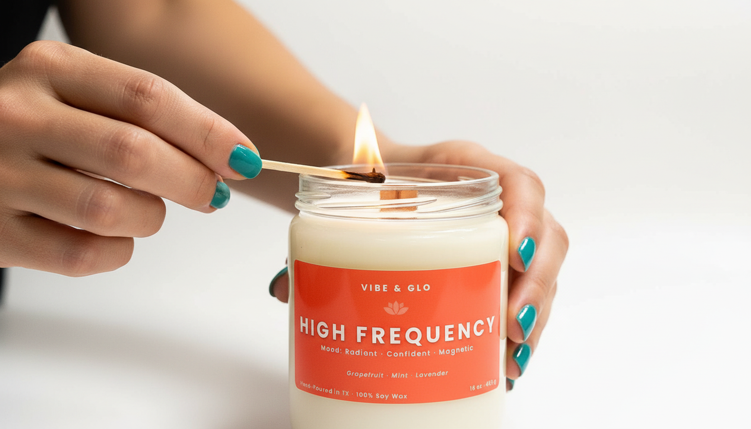 Hand lighting the Vibe & Glo High Frequency wooden wick soy candle with a match, featuring a clear glass jar and bright, uplifting citrus-mint fragrance.