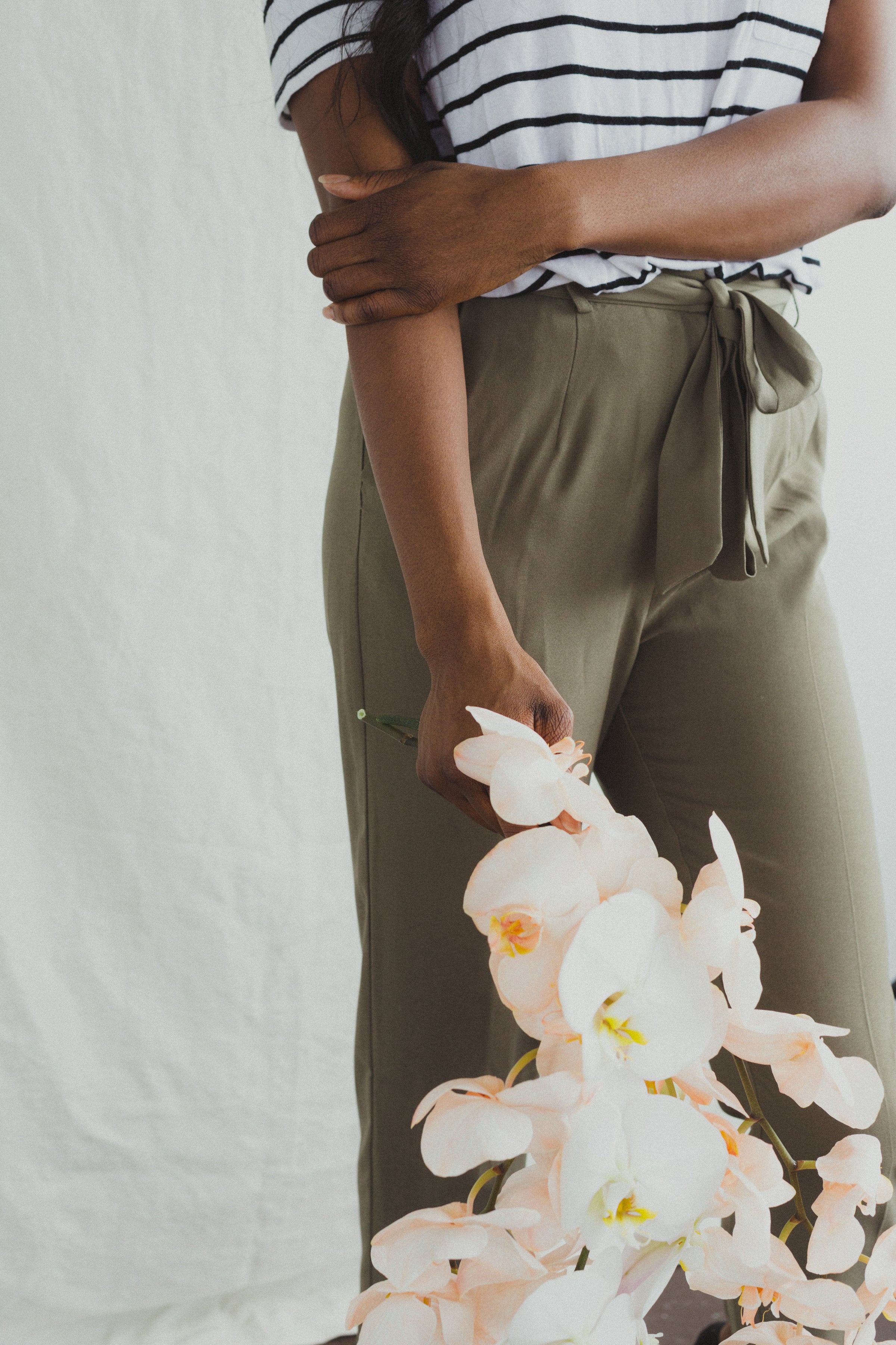 a woman in olive colored stylish pants holding a bunch of orchids