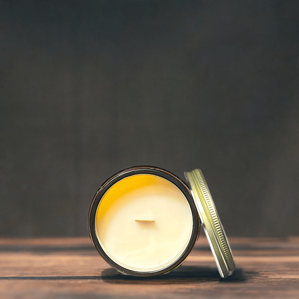 
                      
                        The image displays a close-up of an open bourbon wood wick candle on a dark wooden surface. The candle has a smooth, creamy wax with a single wick in the center, and its metal lid is casually placed beside it, slightly out of focus. The background is dark and muted, emphasizing the candle and creating a calm, serene atmosphere. The simplicity of the composition focuses attention on the texture and color of the candle wax.
                      
                    