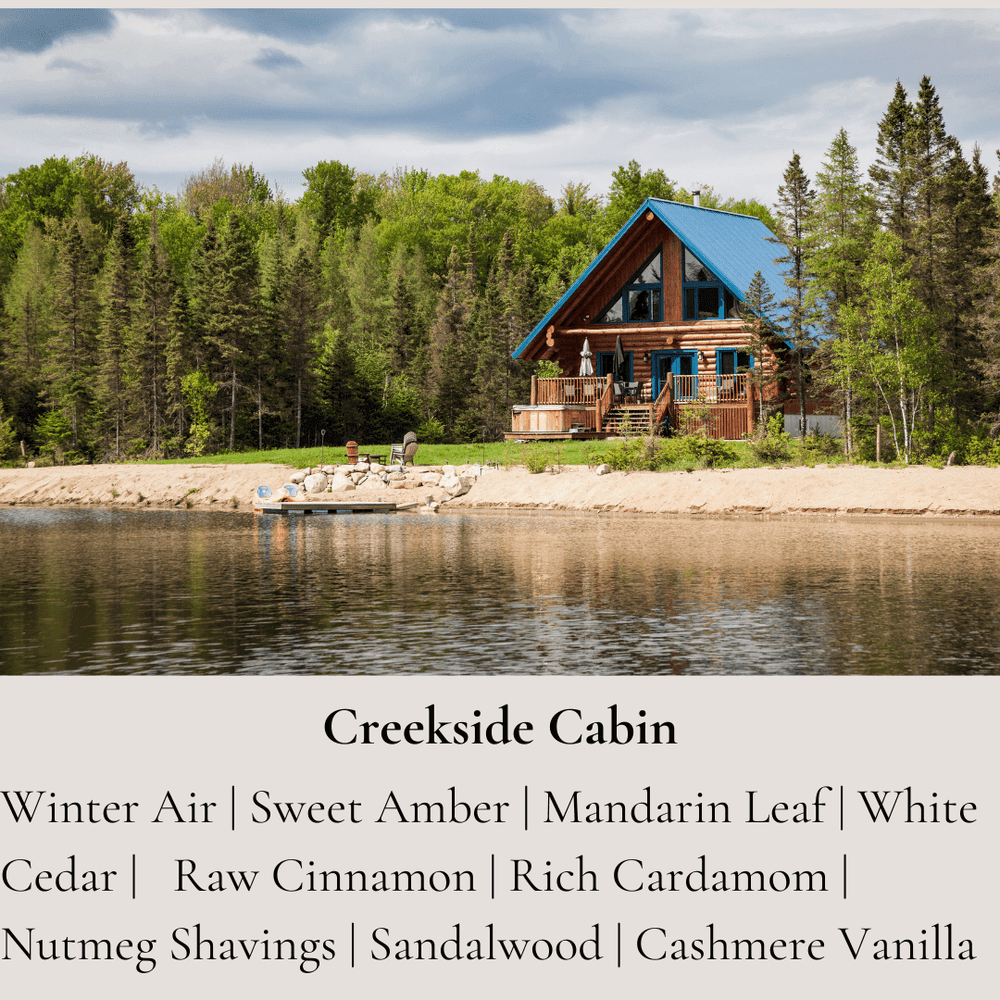 
                      
                        A serene cabin by the creek, surrounded by dense greenery, reflecting in the calm water. Below the image is a text description of the "Creekside Cabin" candle's scent notes, which include winter air, sweet amber, white cedar, sandalwood, and cashmere vanilla, among others.
                      
                    