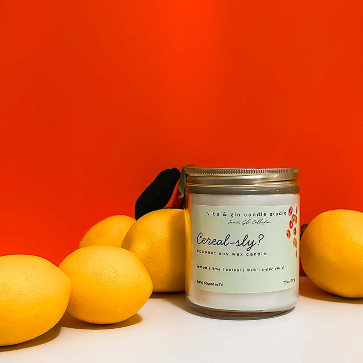 Cereal-sly? coconut soy wax candle with lemon, lime, and cereal milk. Styled with lemons on a vibrant orange backdrop.