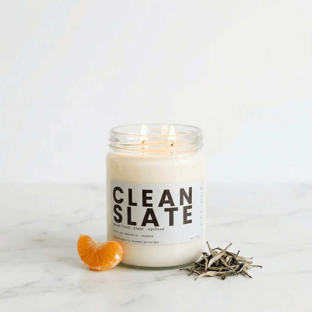 Clean Slate candle with mandarin slice and white tea leaves on marble surface, fresh clean home fragrance candle