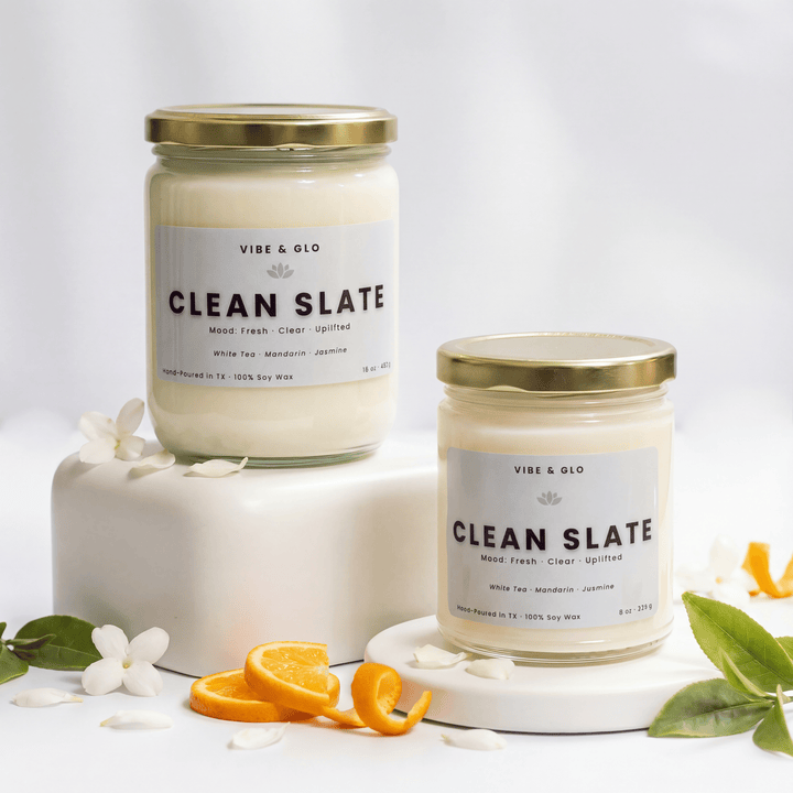 Clean Slate white tea, mandarin, and jasmine soy candles in 16 oz and 8 oz jars with gold lids, styled with orange slices and white florals.