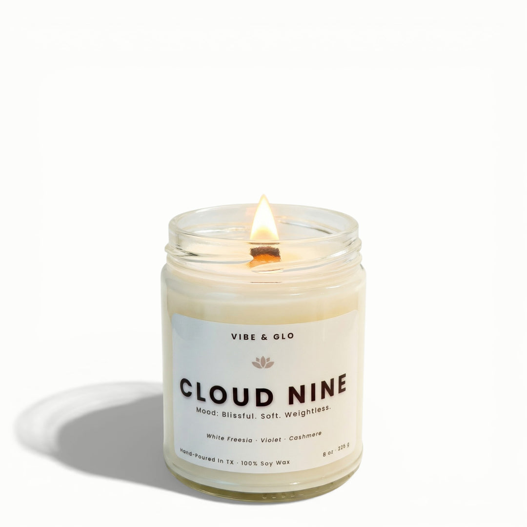 Cloud Nine white freesia and cashmere soy candle by Vibe & Glo with lit wooden wick in minimalist clear glass jar.