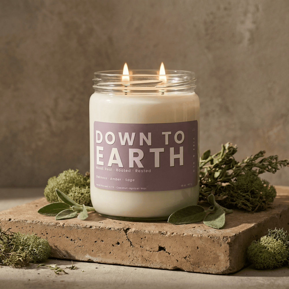 Down to Earth 2-wick soy candle styled on stone with moss and sage, highlighting earthy amber and herbal fragrance notes