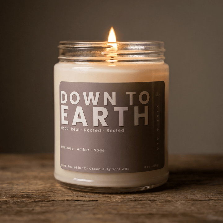Down to Earth candle glowing on a wooden surface with warm ambient lighting highlighting amber and sage notes