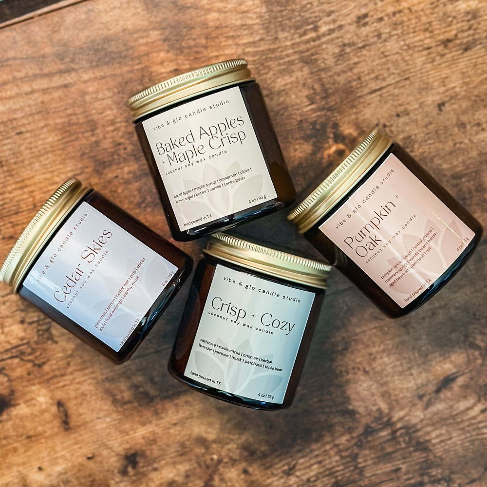 Flatlay of Vibe & Glo Fall Candle Flight, 4-piece fall candle discovery set with wood wick candles in amber jars.