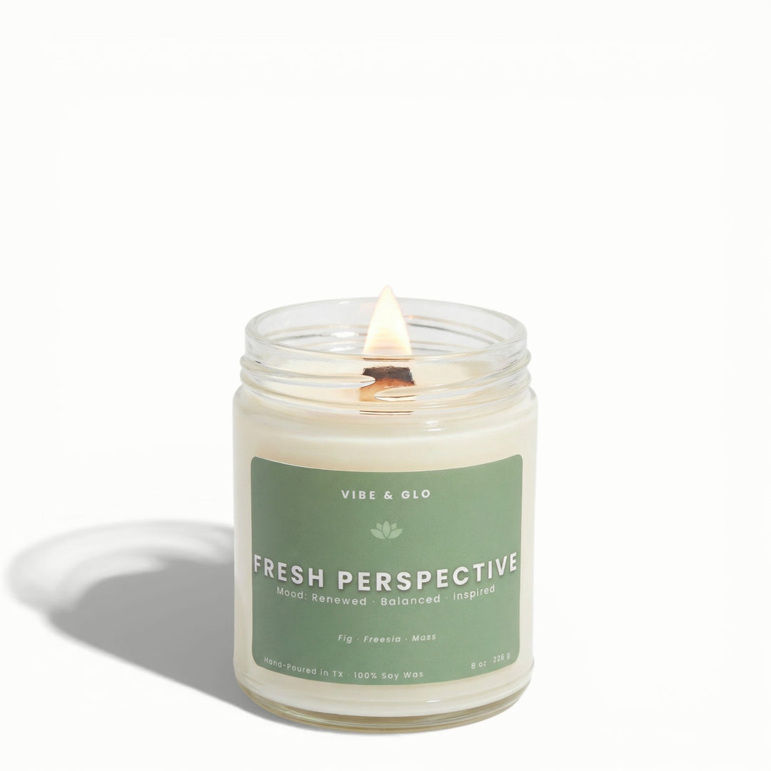 Fresh Perspective fig, freesia, and moss soy candle by Vibe & Glo with lit wooden wick on white studio background.