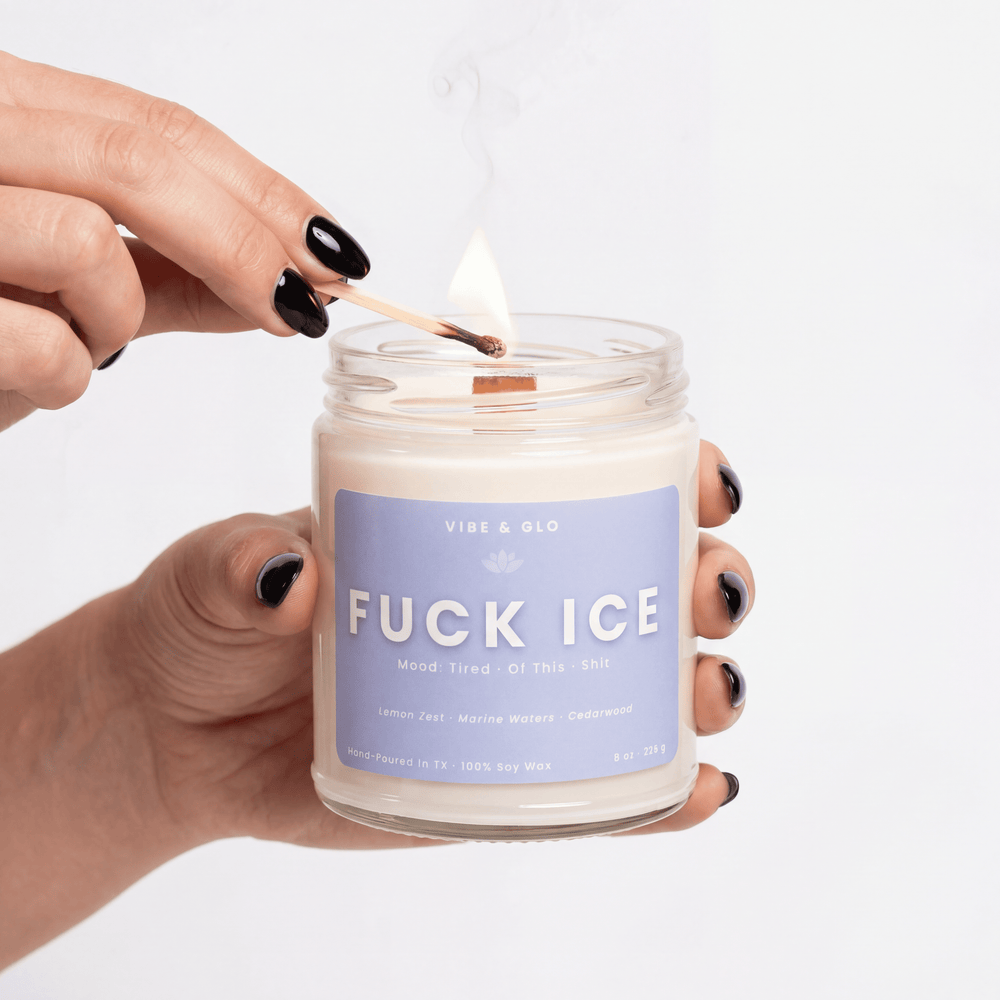Candle labeled 'FUCK ICE' being lit with a match, on a plain background