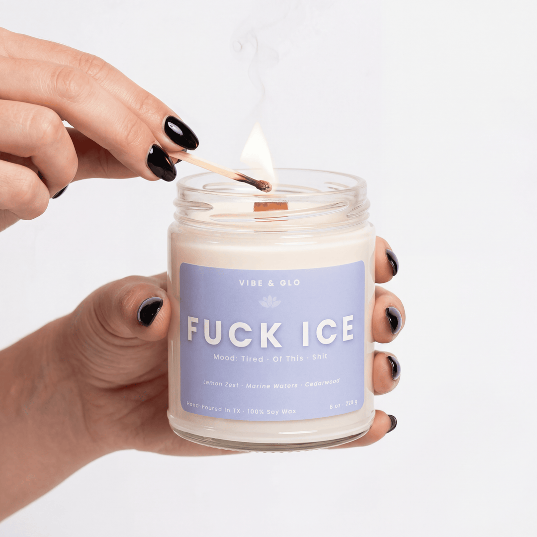 Candle labeled 'FUCK ICE' being lit with a match, on a plain background