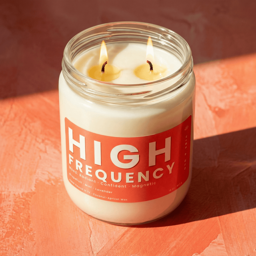 High Frequency 2-wick soy candle burning with two cotton wicks, close-up of clean melt pool and bright orange label in warm light