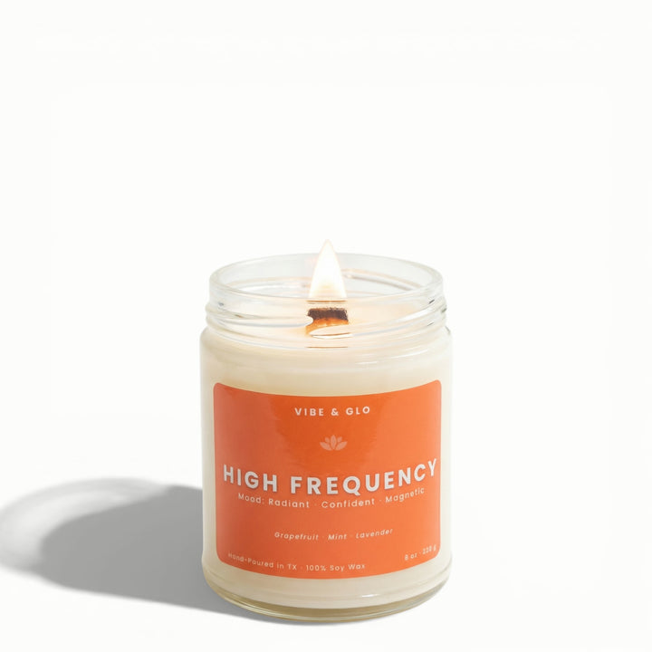 High Frequency grapefruit, mint, and lavender soy candle by Vibe & Glo featuring a lit wooden wick in clear jar.