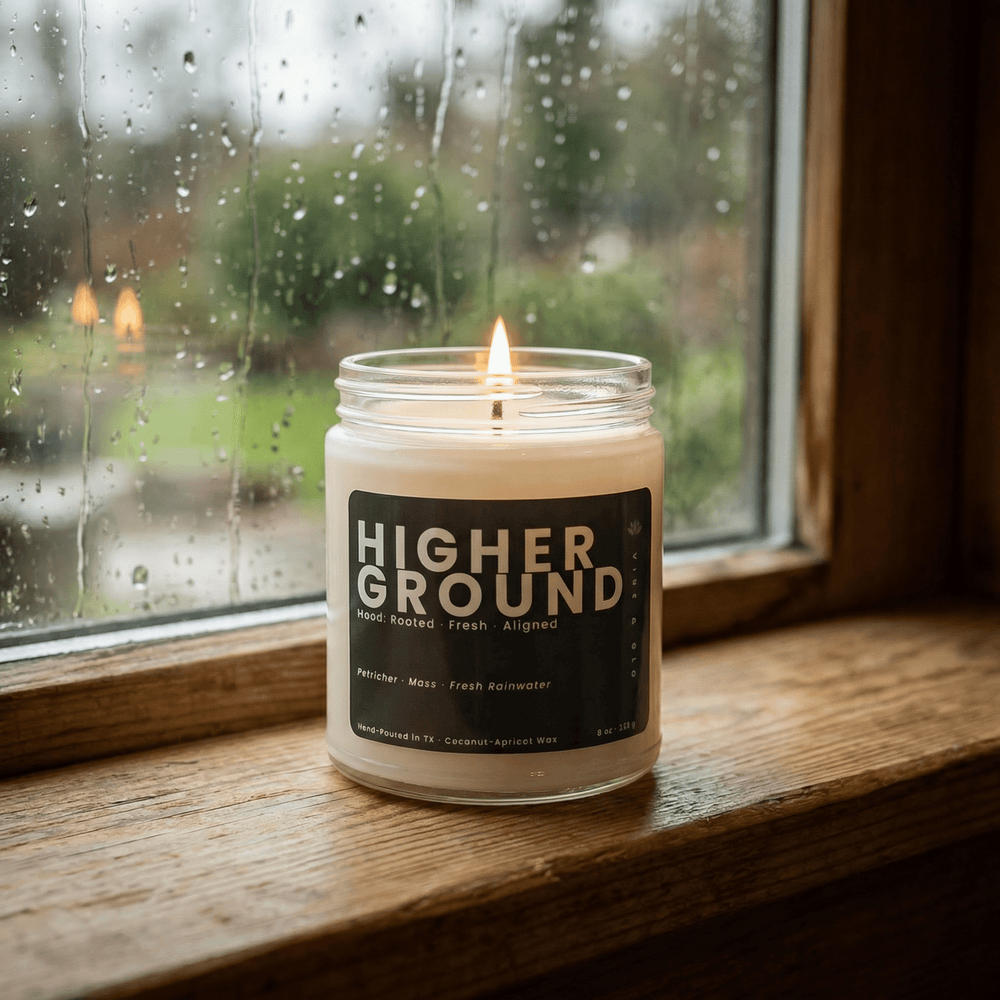 Higher Ground jar candle burning by rainy window on wood sill, clean fresh rain inspired scent creating a cozy grounded atmosphere