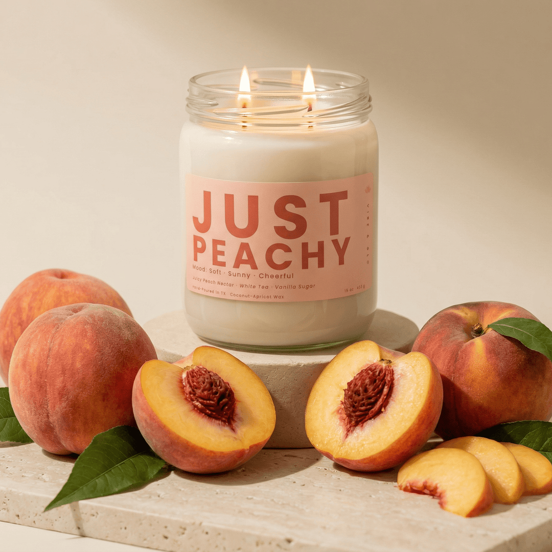 Just Peachy candle displayed with whole and sliced peaches on stone pedestal, fruity soy candle with soft warm aesthetic