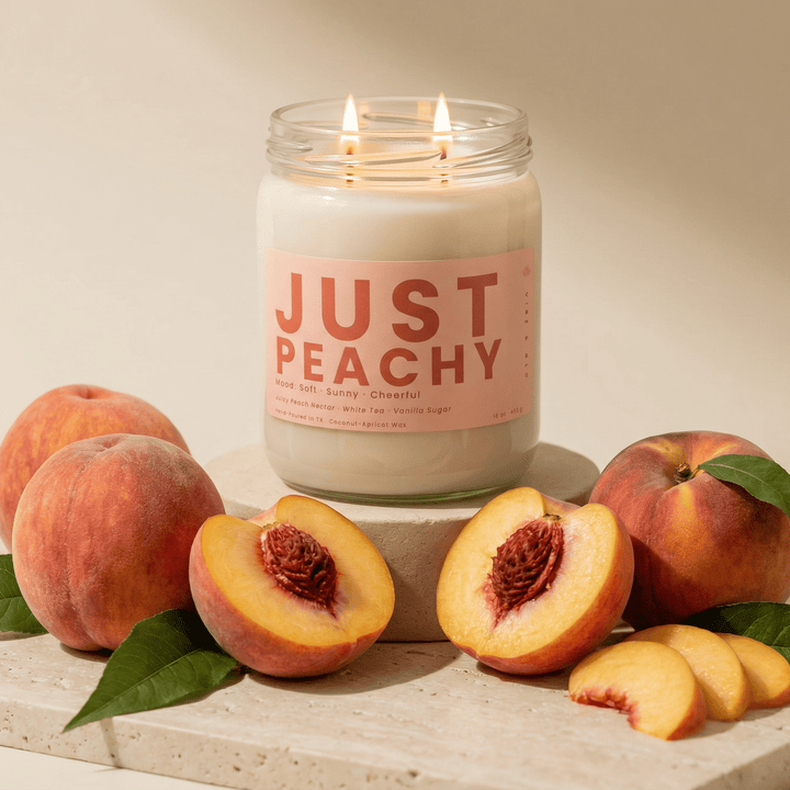 Just Peachy candle displayed with whole and sliced peaches on stone pedestal, fruity soy candle with soft warm aesthetic