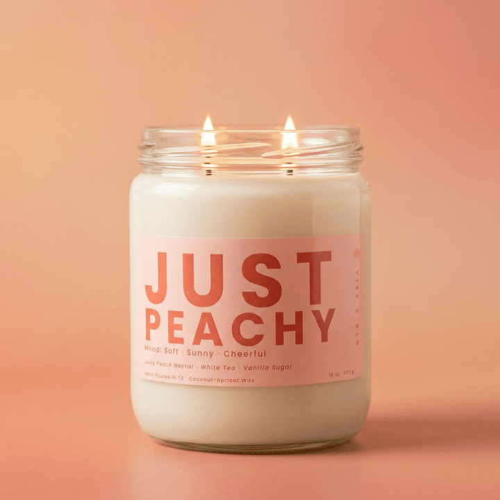 Just Peachy 2-wick candle glowing against peach background, soft fruity candle with peach nectar and vanilla sugar scent