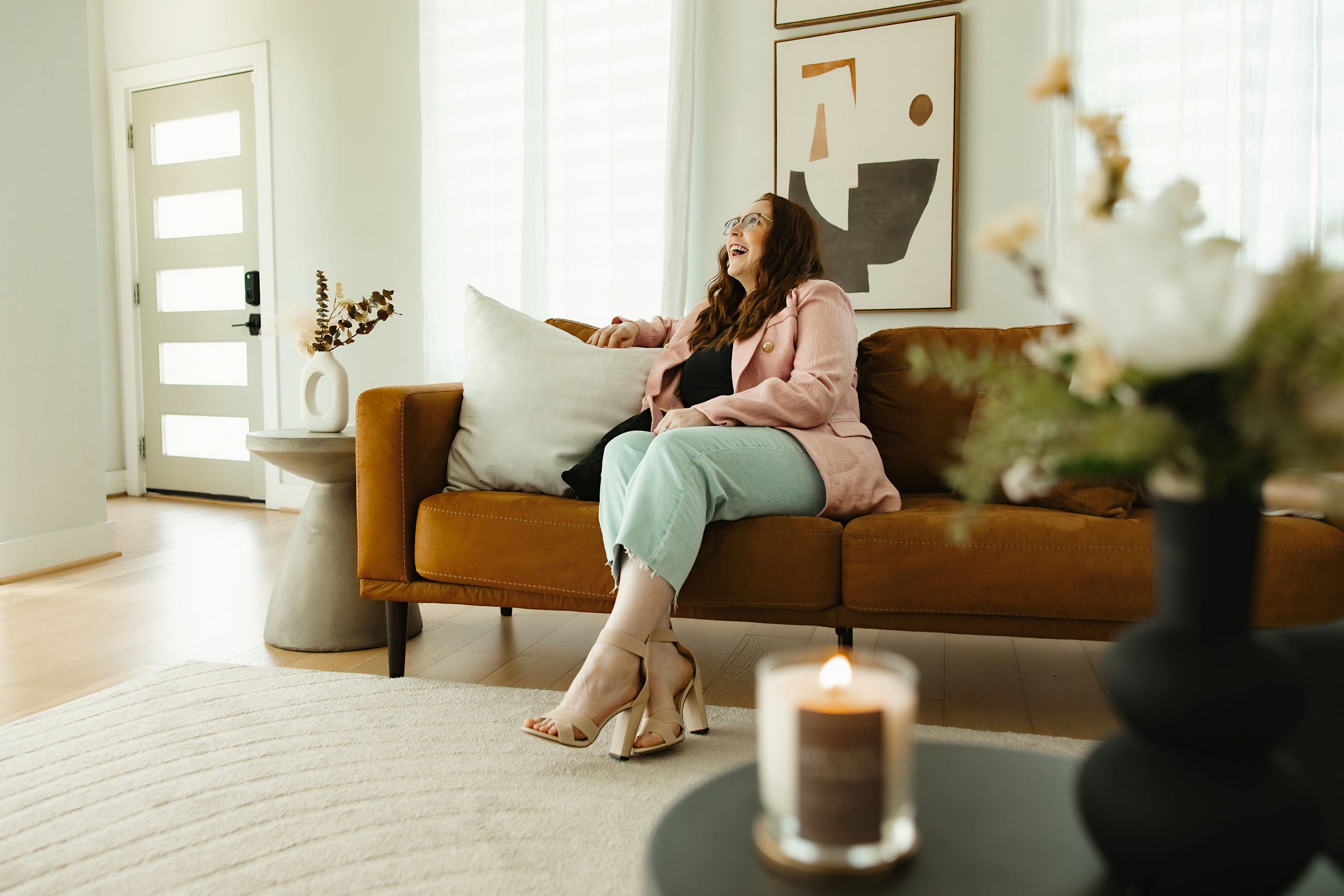 Woman sitting on a brown couch in a living room with a candle and decorative items.