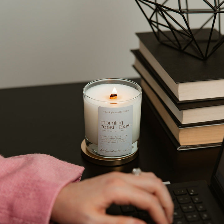 Morning Roast + Toast candle lit on a desk with books, evoking a cozy, warm ambiance.