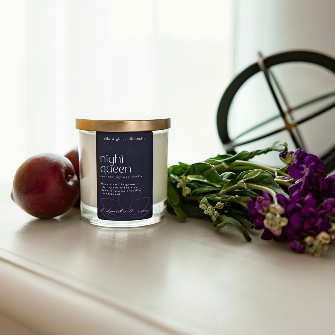 Night Queen candle by Vibe & Glo on a white tabletop, styled with a plum and fresh purple flowers.