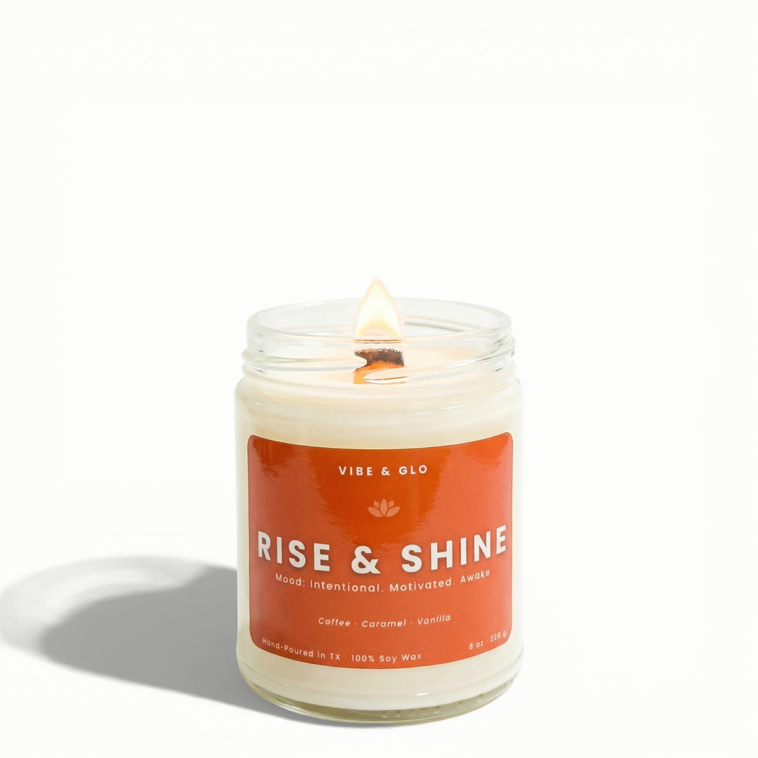Rise & Shine coffee, caramel, and vanilla soy candle by Vibe & Glo with lit wooden wick on white background.