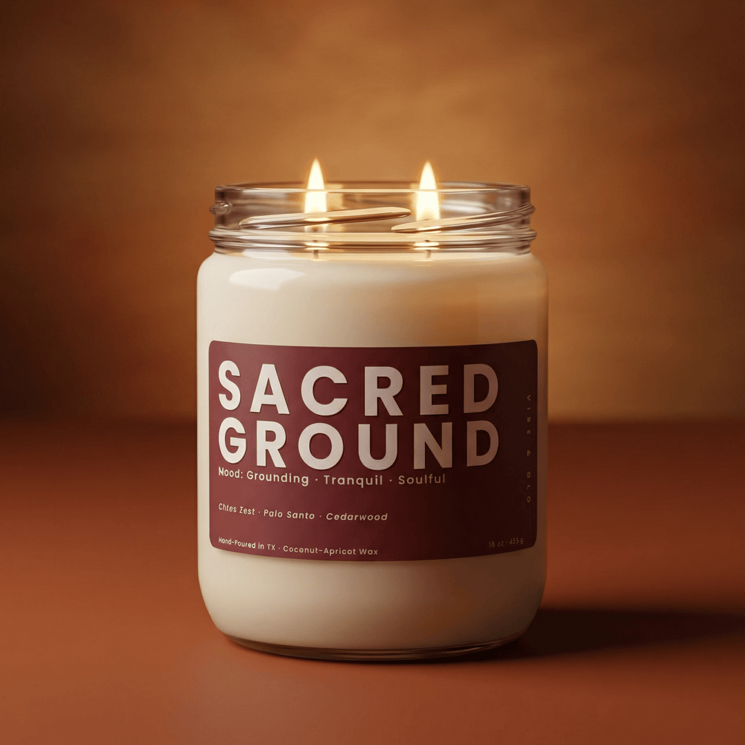 Sacred Ground 2-wick candle burning against a warm amber background, clean modern product image