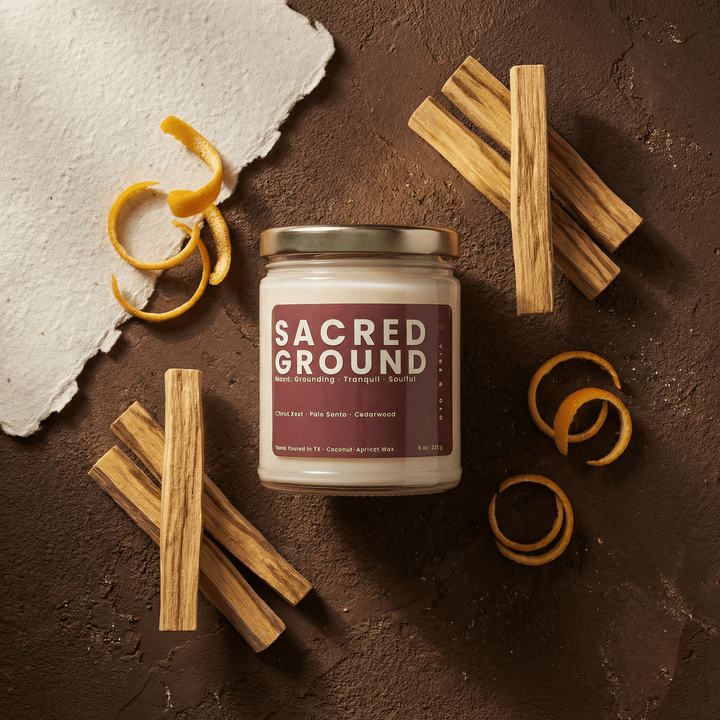 Flatlay of Sacred Ground woody candle with palo santo sticks and citrus peel highlighting cedarwood and grounding scent notes