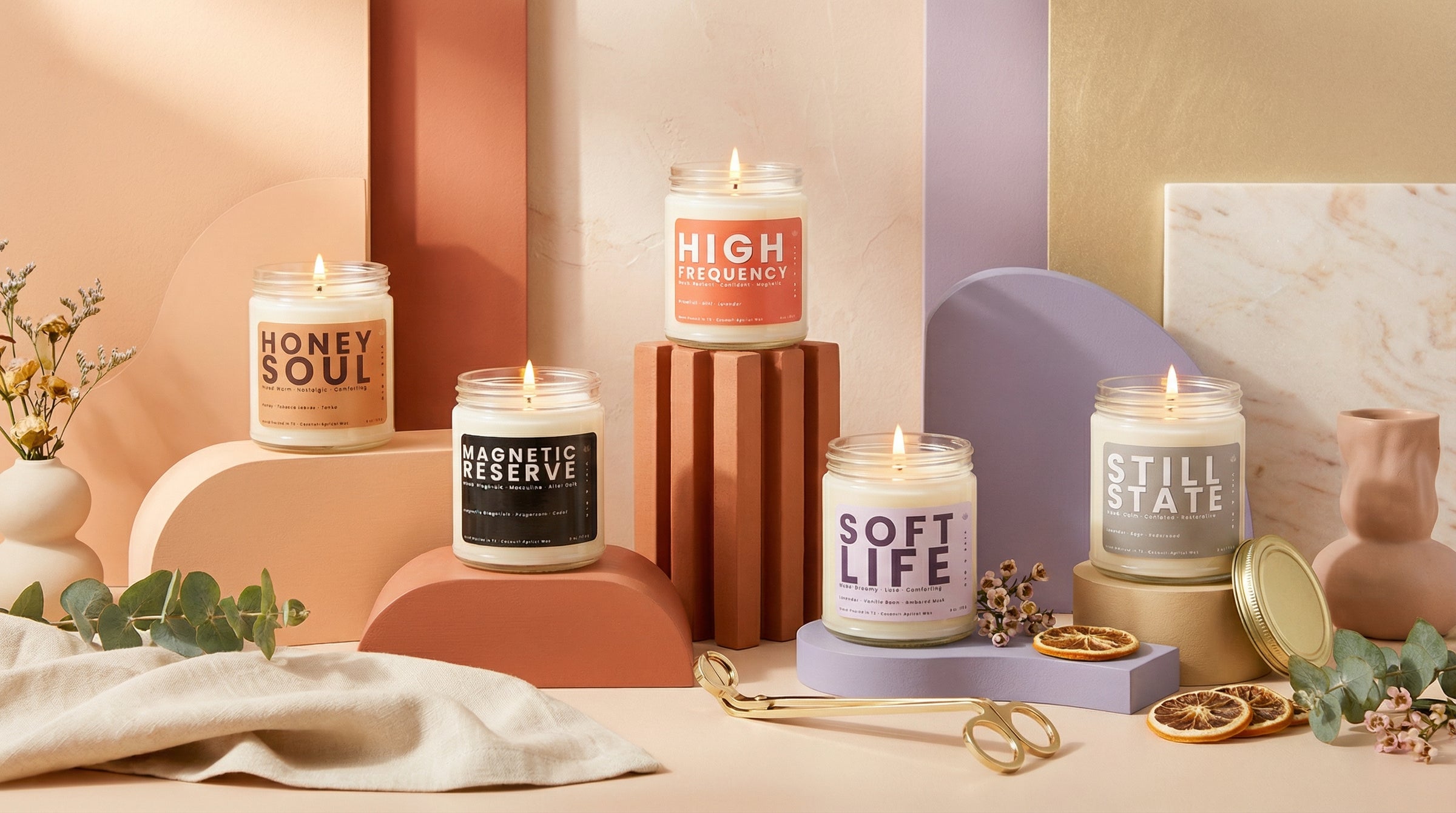 Signature Jar Candle collection featuring multiple clean burning candles in coconut apricot wax displayed on modern pedestals with warm colorful backdrop