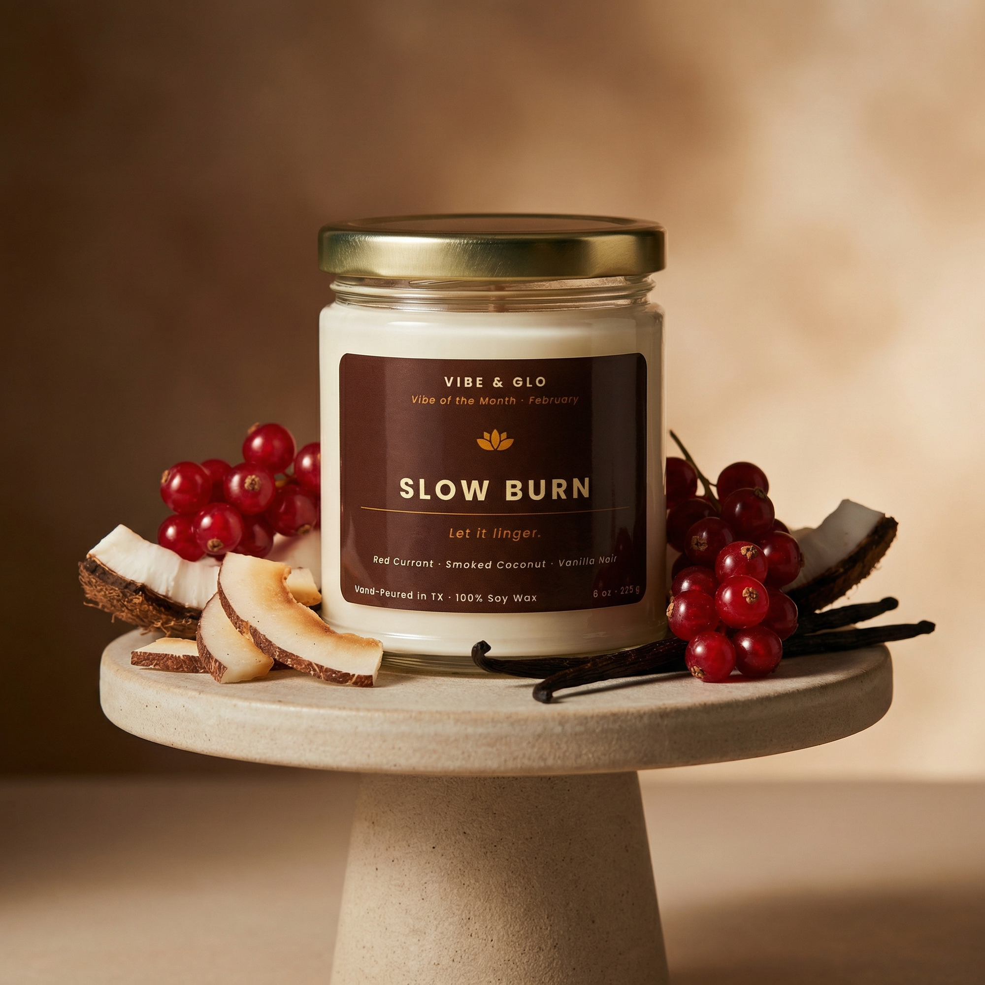 Vibe & Glo “Slow Burn” coconut vanilla candle from a monthly candle subscription, featuring a lit soy candle on a pedestal with coconut pieces, red currants, and vanilla beans in a warm, minimalist setting.