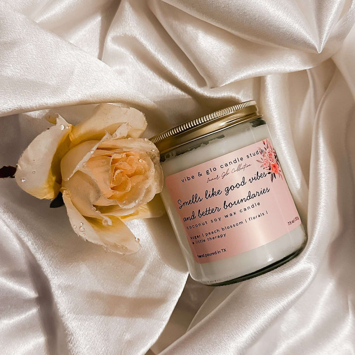 Smells like good vibes and better boundaries coconut soy wax candle with sugar, peach blossom, and florals. Styled on white satin with a peach rose for an elegant, romantic look.