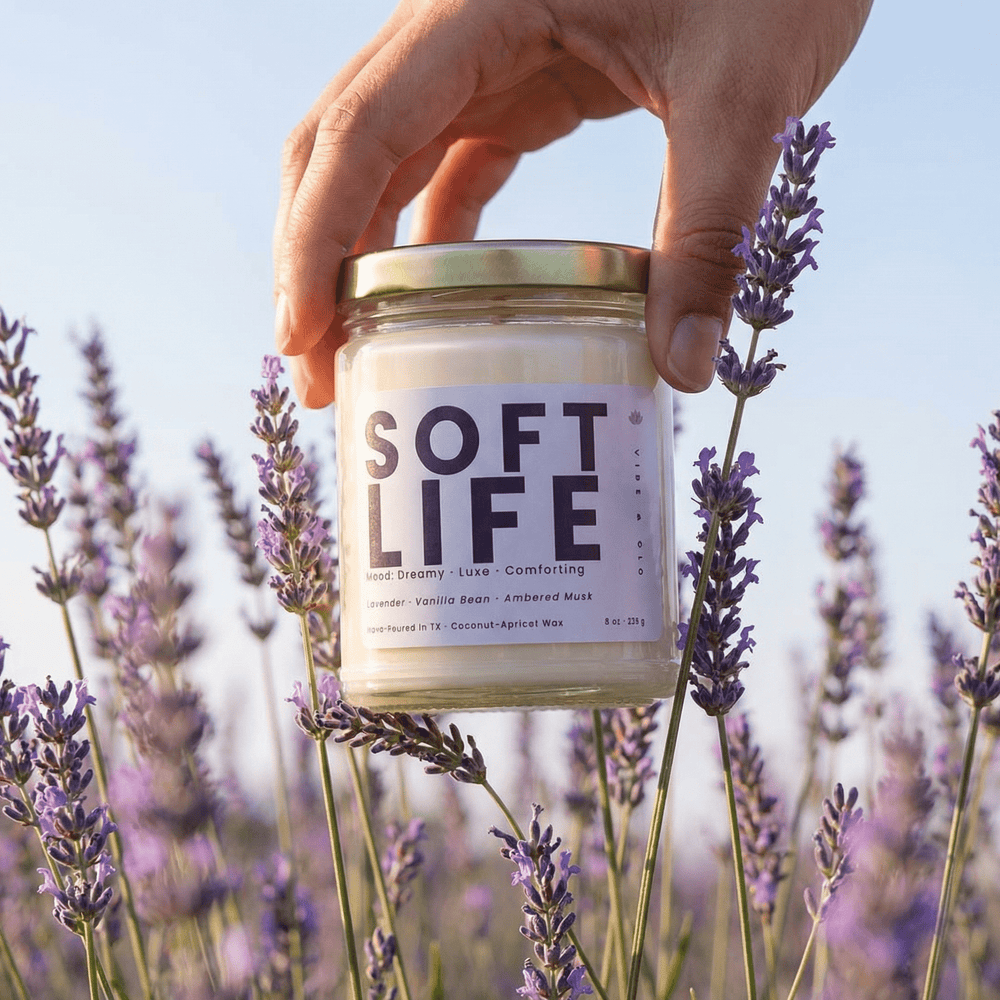Soft Life candle held in a lavender field capturing a dreamy relaxing self care moment with a lavender vanilla scented home fragrance