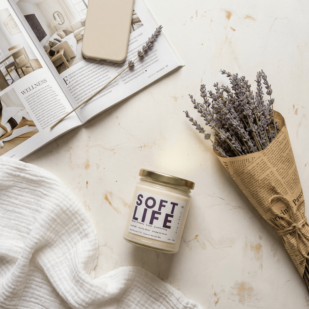 Soft Life candle styled with lavender bundle and open magazine creating a cozy calming home aesthetic with a soft floral scent