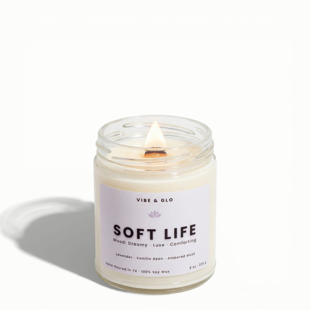 Soft Life lavender, vanilla bean, and ambered musk soy candle by Vibe & Glo with lit wooden wick in clear jar.