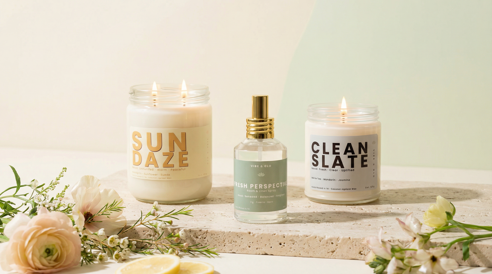 Vibe & Glo spring candle collection featuring Sun Daze and Clean Slate candles with a Fresh Perspective room and linen spray, styled with soft florals and citrus on a textured stone surface with a light green gradient background.