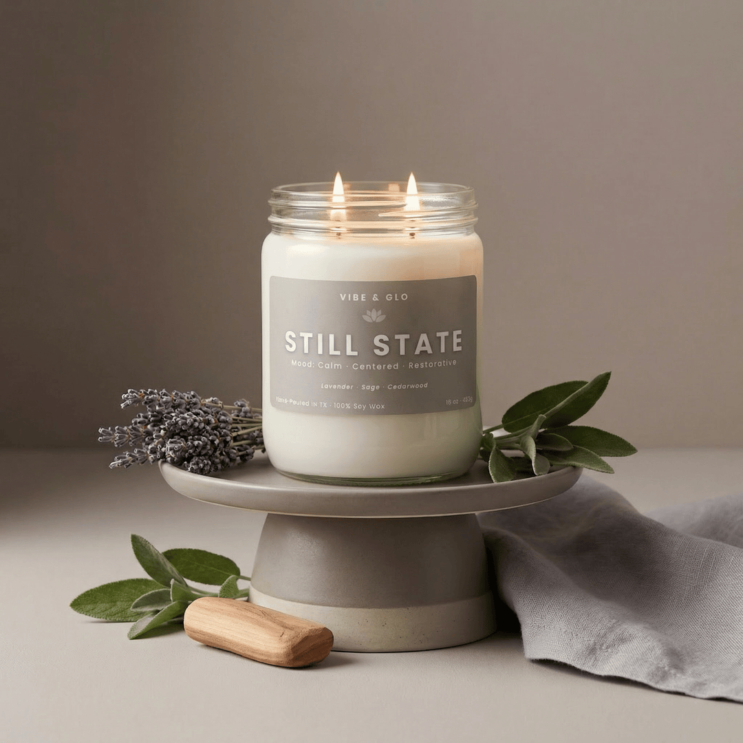 Lit Still State double wick soy candle with lavender and sage accents displayed on a ceramic pedestal, creating a soft, calming home fragrance scene.