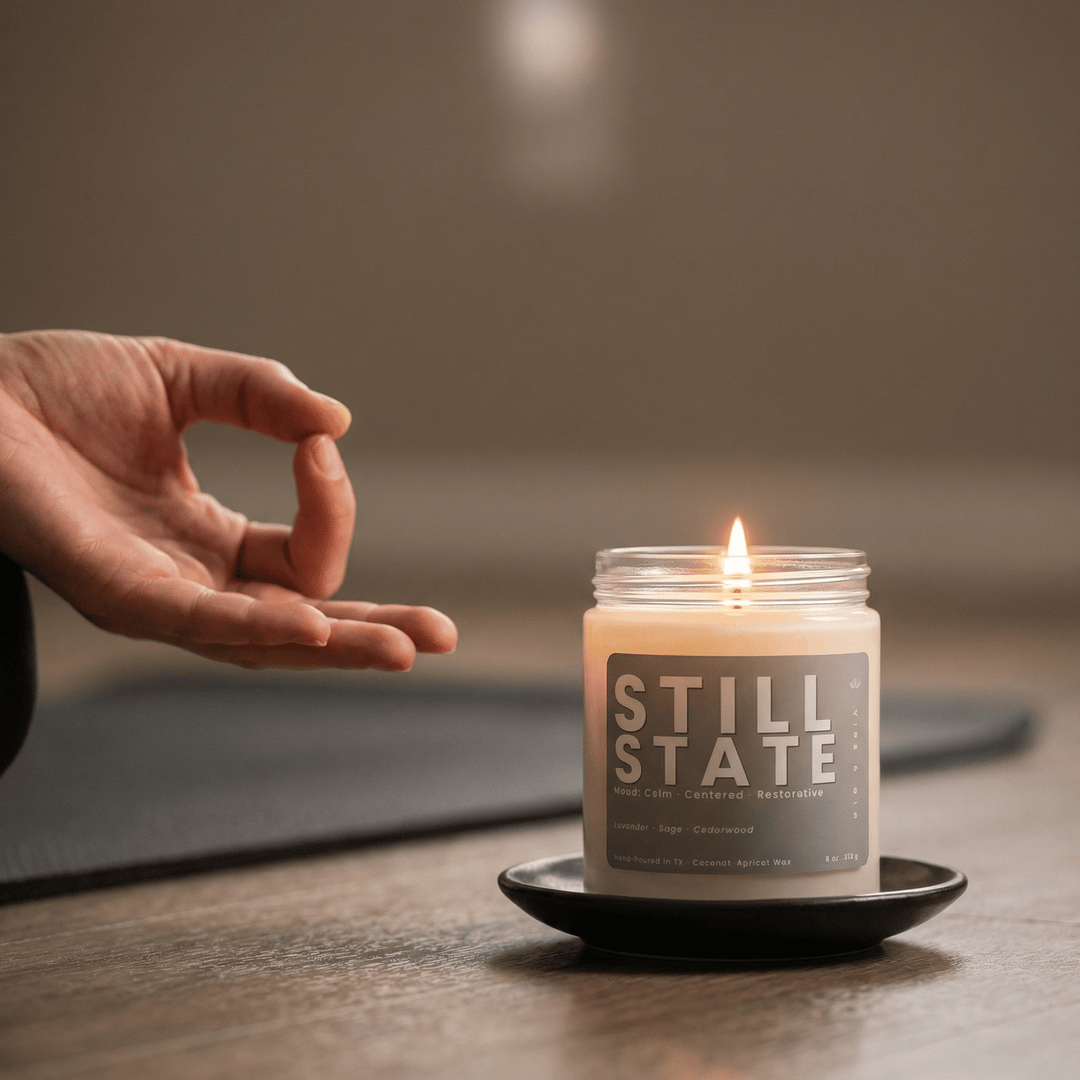 Lit Still State candle beside a meditation hand pose creating a peaceful calming ritual environment