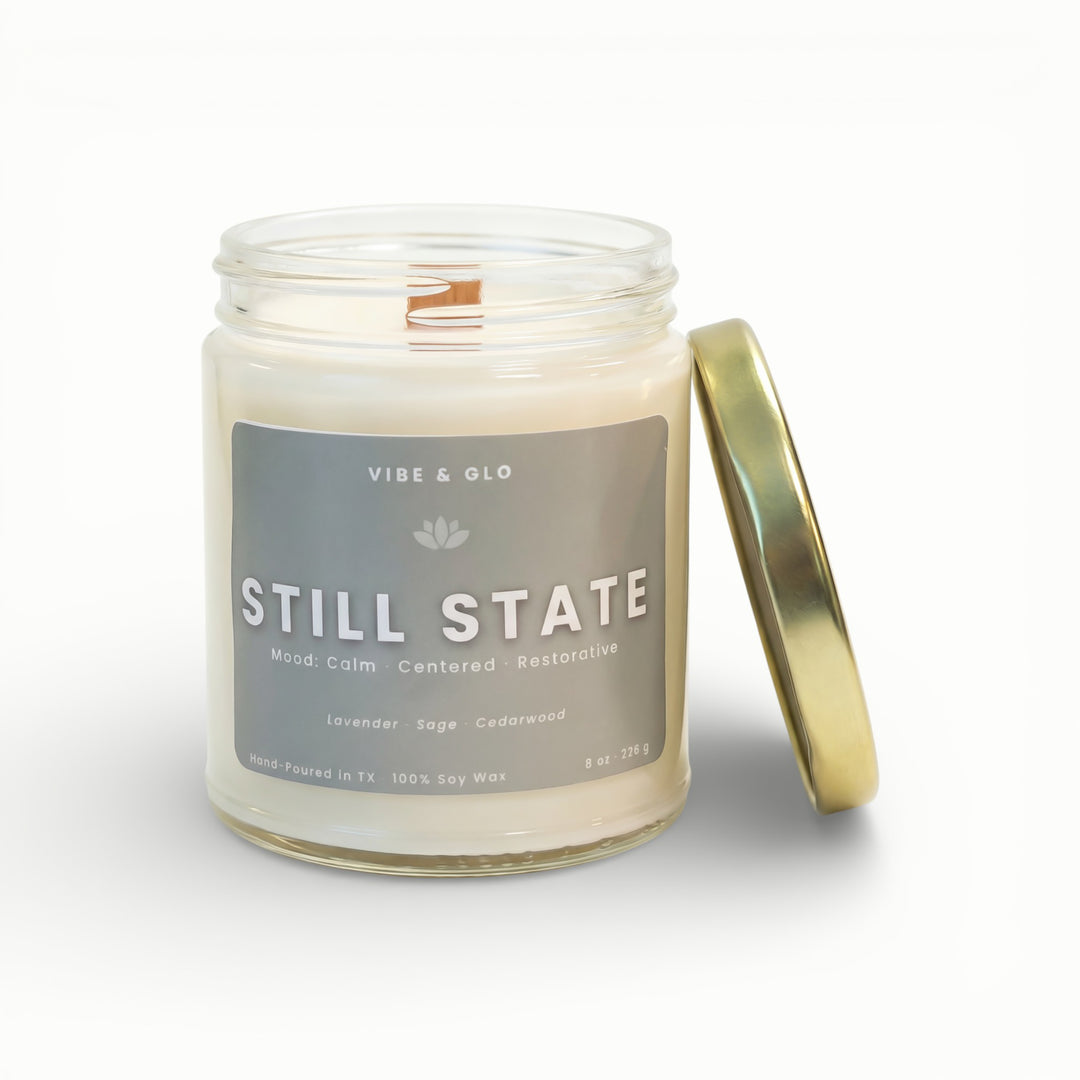 Vibe & Glo Still State soy candle in clear glass jar with wooden wick and gold lid, lavender sage and cedarwood fragrance for a calming mood
