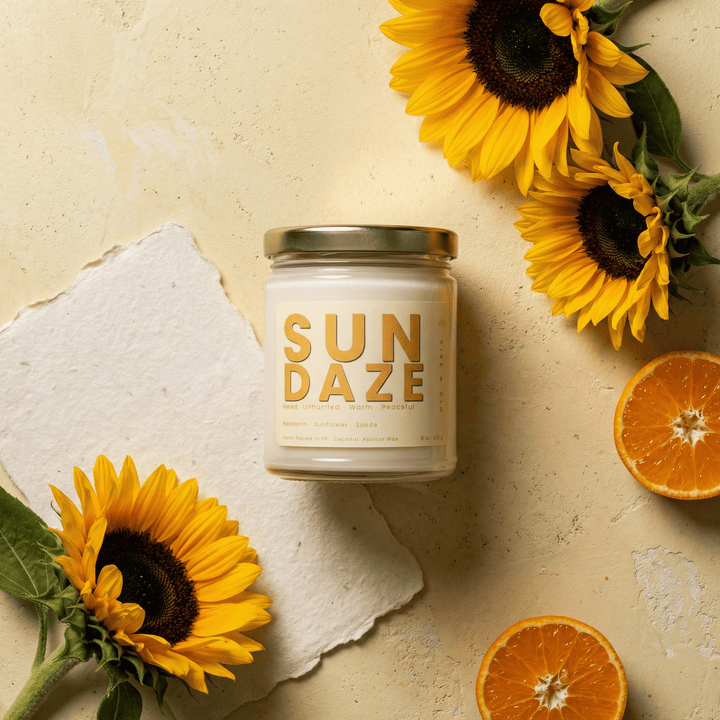 Sun Daze candle styled with sunflowers and citrus slices in a warm flatlay creating a bright uplifting home fragrance aesthetic