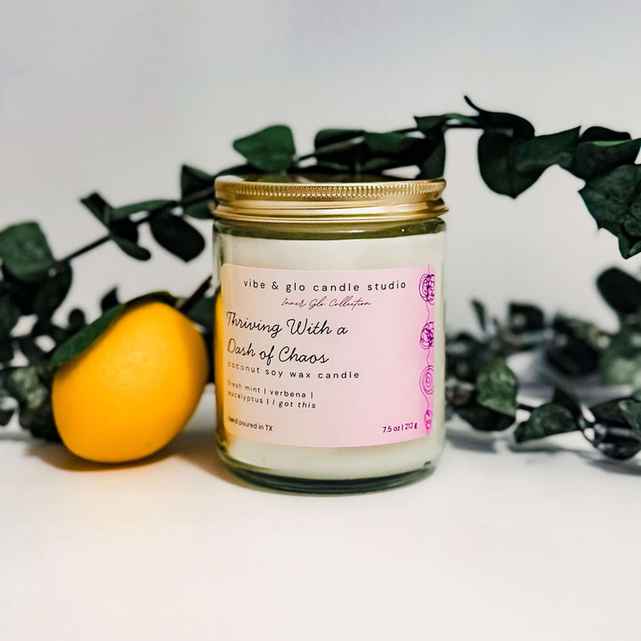 Thriving With a Dash of Chaos coconut soy wax candle with fresh mint, verbena, and eucalyptus. Close-up with lemon and greenery for a bright, uplifting look.